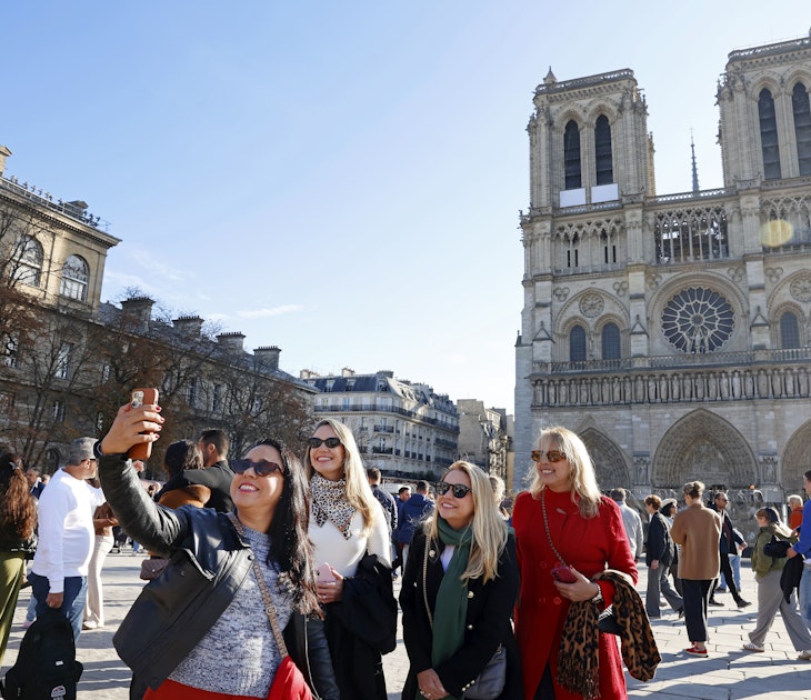 PARIS, FRANCE - OCTOBER 25: Tourists take a selfie with Notre-Dame de Paris Cathedral a few weeks before its reopening to the public scheduled for December 7, 2024 on October 25, 2024 in Paris, France. French ministers have floated the idea of â€‹â€‹charging tourists to enter the world-famous Notre Dame Cathedral in Paris when it opens on December 7 after five years of restoration. 